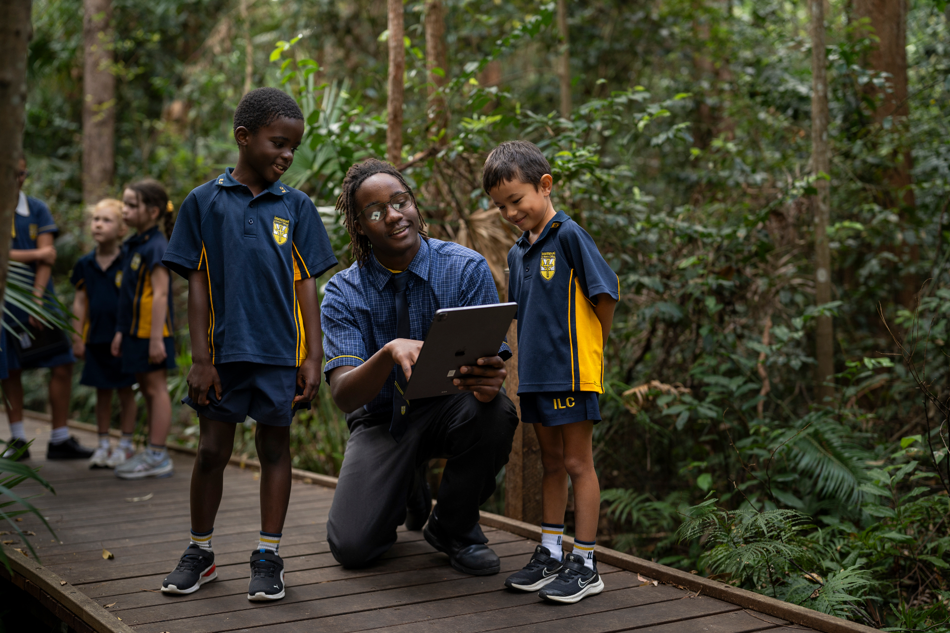 A senior student guiding two primary students with a tablet on a rainforest boardwalk at Immanuel Lutheran College